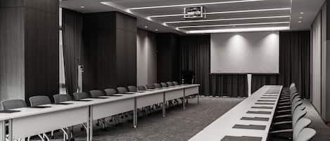 A conference room with a long table, chairs, a projector screen, and a carpeted floor.