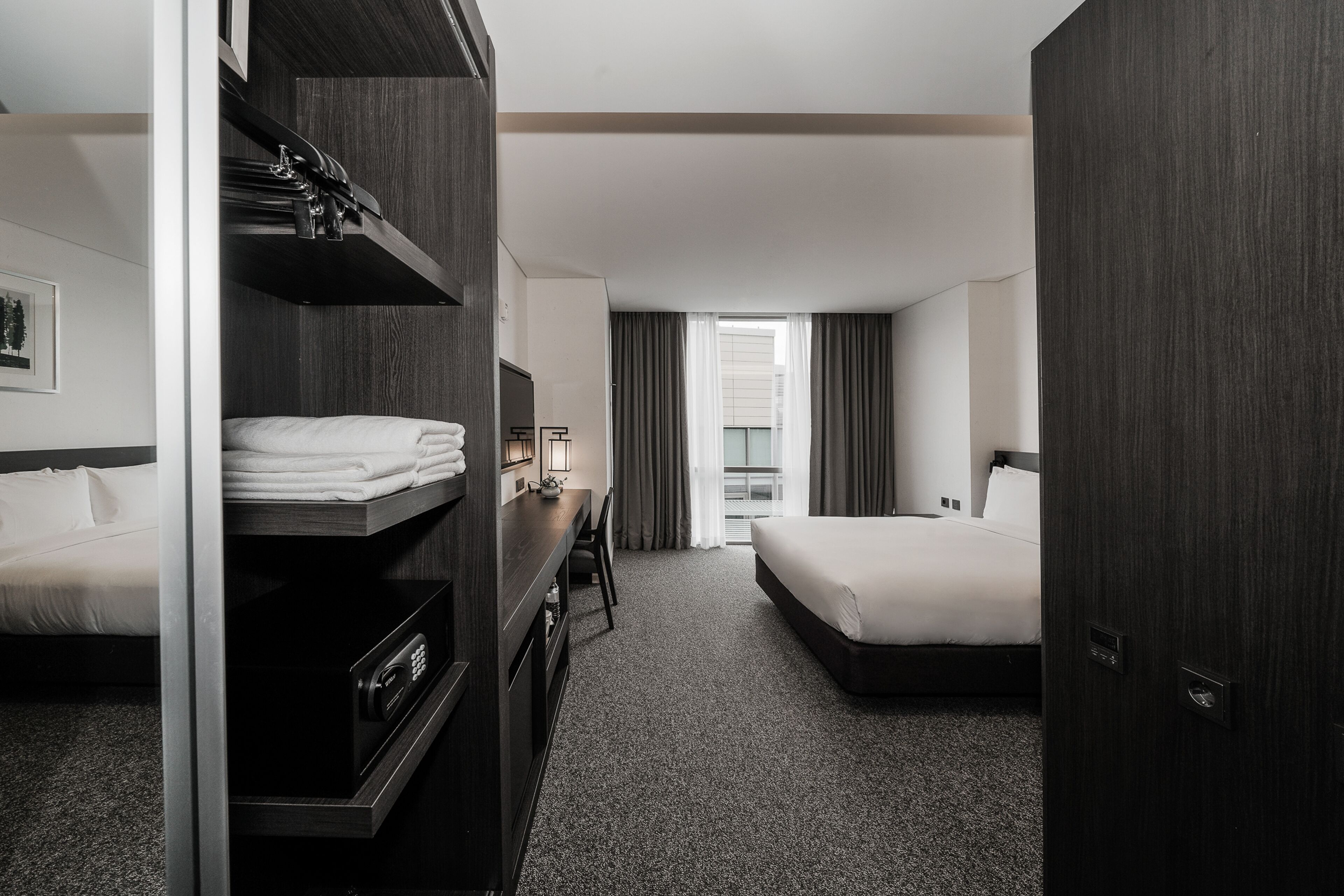 A hotel room with a bunk bed, a desk with a computer, a TV, and a large window with curtains.