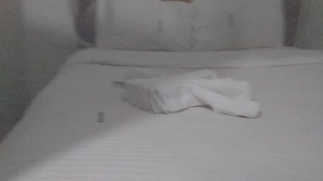 A neatly made bed with a folded white towel and a small rectangular object on the bed.