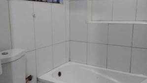 A bathroom with white tiles, a bathtub, and a toilet. - Vegas Hotel (Kampala)
