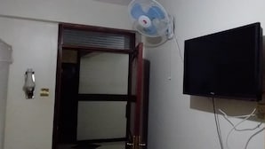 A room with a closed door, a wall-mounted TV, and a standing fan. - Vegas Hotel (Kampala)