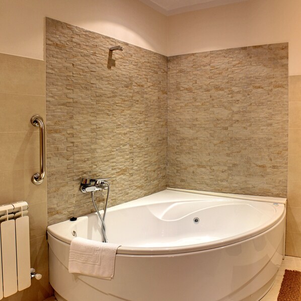 A large, curved bathtub with a showerhead and grab bar, set against a textured stone wall. - La Montaña Mágica (Llanes)