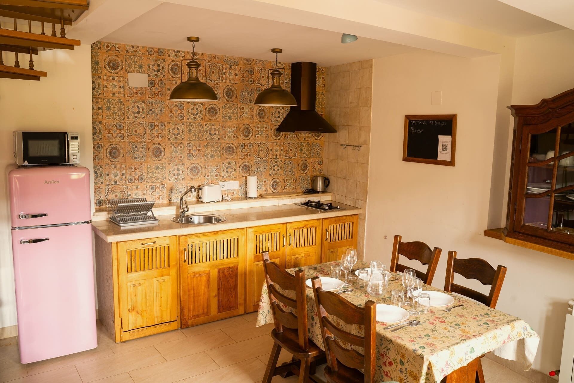 A kitchen with a pink refrigerator, wooden cabinets, a dining table set for four, and a patterned backsplash.