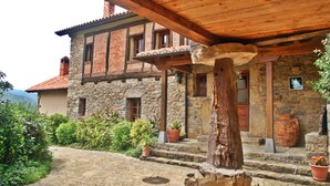Edifici de pedra amb un porxo de fusta, plantes en testos i un aspecte rústic.