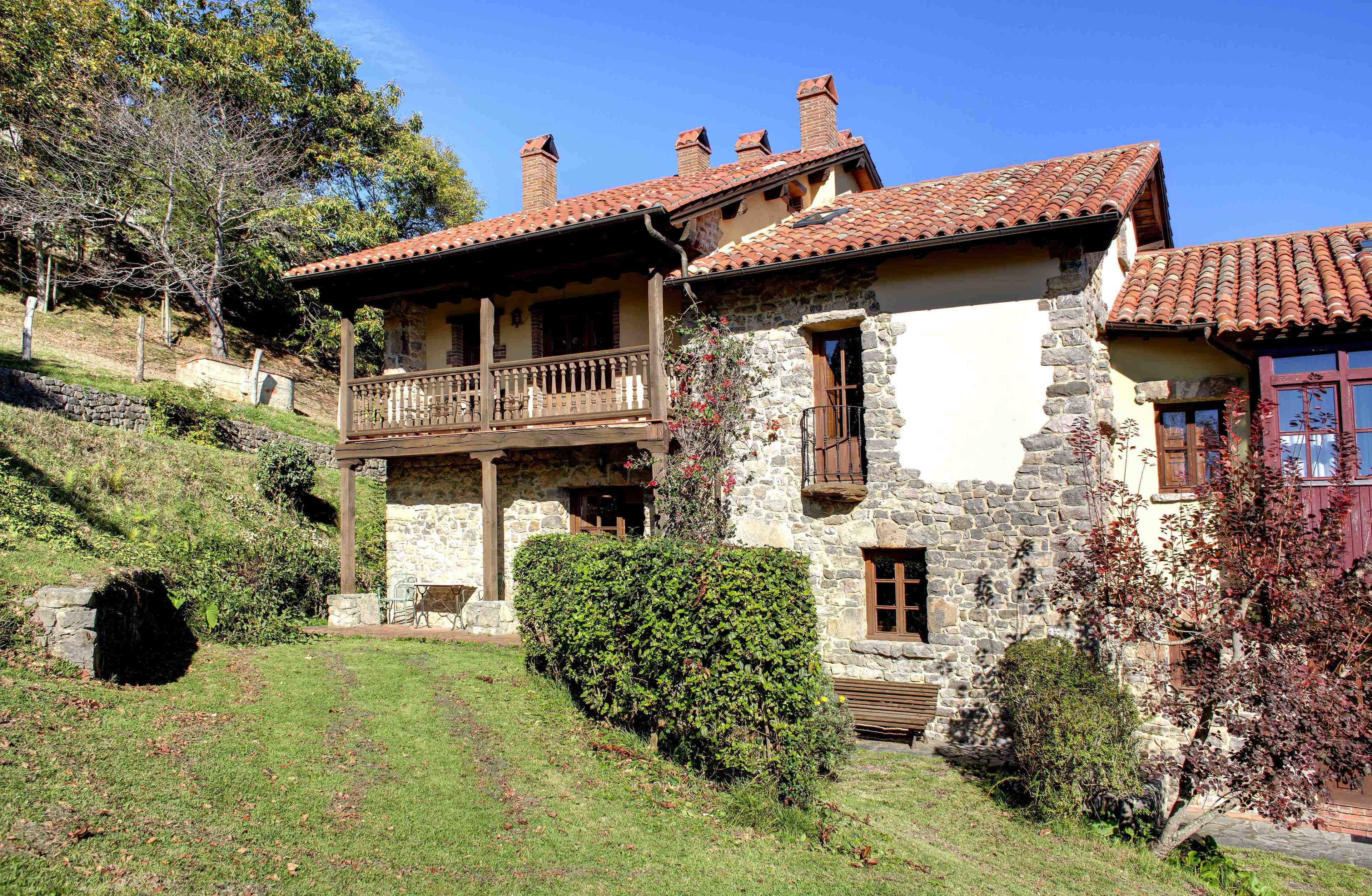 Una casa de piedra con balcón, una escalera de piedra y un jardín bien cuidado.