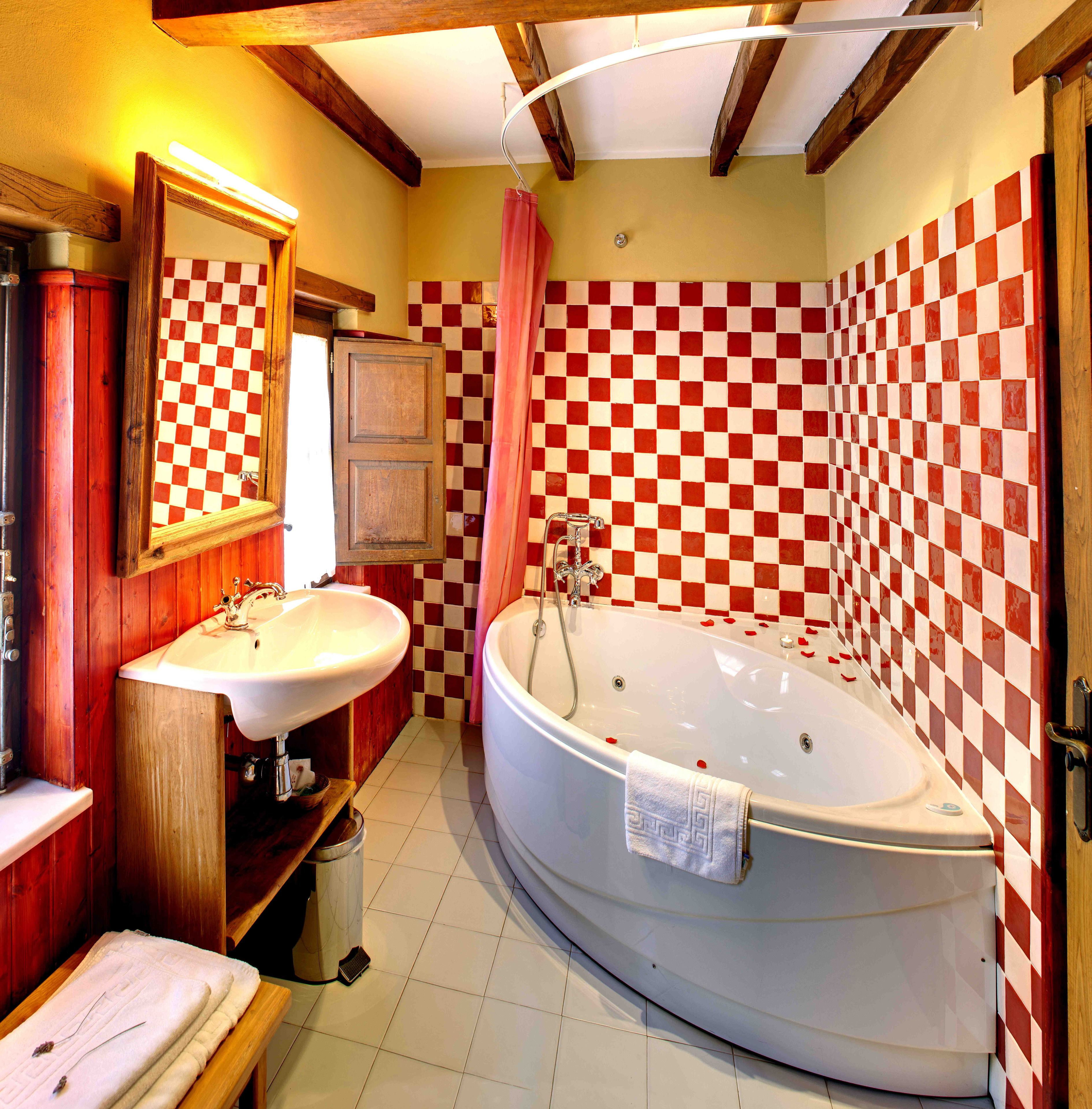 Un baño con pared de baldosas blancas y rojas a cuadros, una bañera grande, un lavamanos y un espejo.