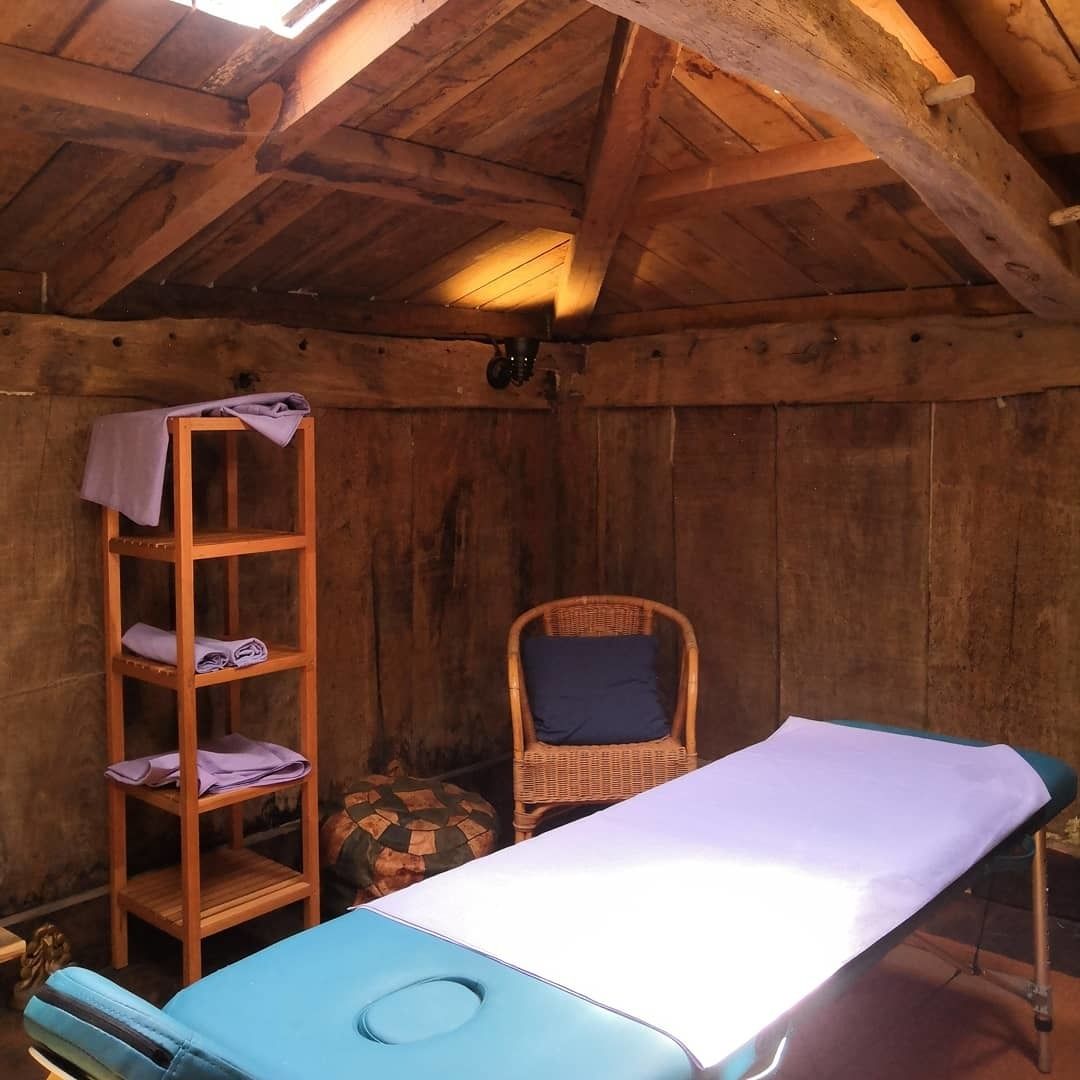 A wooden room with a massage table, a wooden shelf with towels, and a wicker chair.