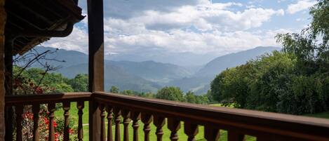 Un balcón de madera con vistas a colinas y montañas verdes.