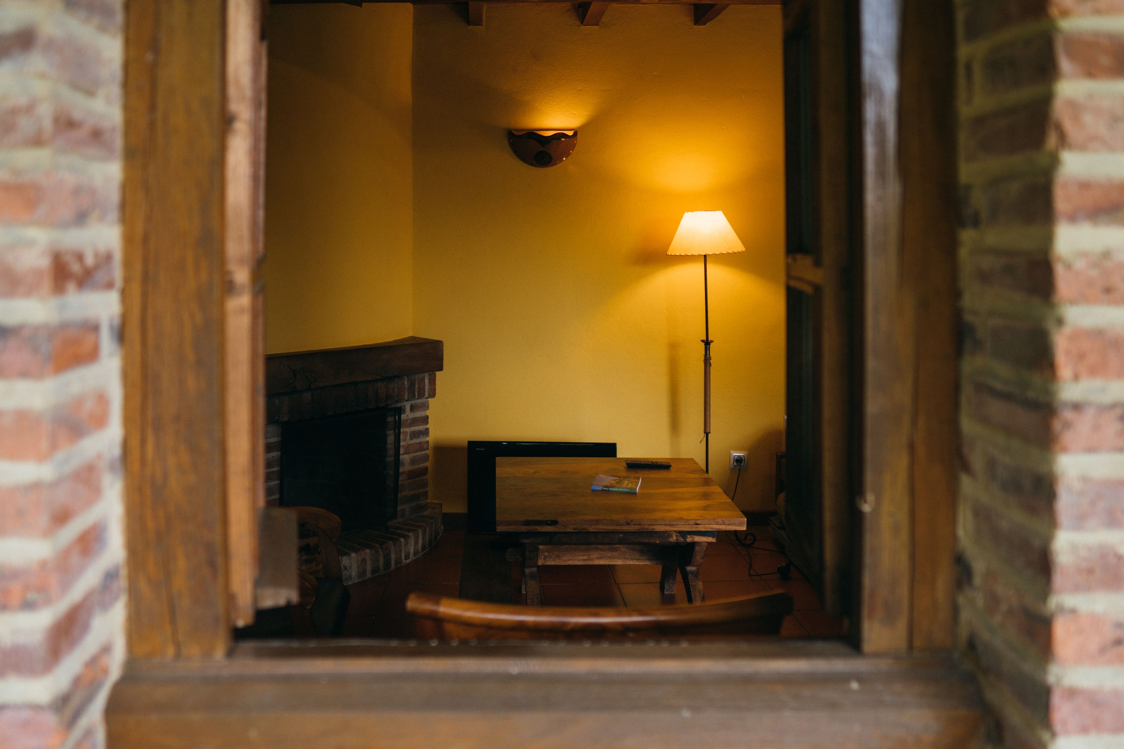 Una habitación acogedora con chimenea de ladrillo, una mesa de madera y una lámpara de pie.