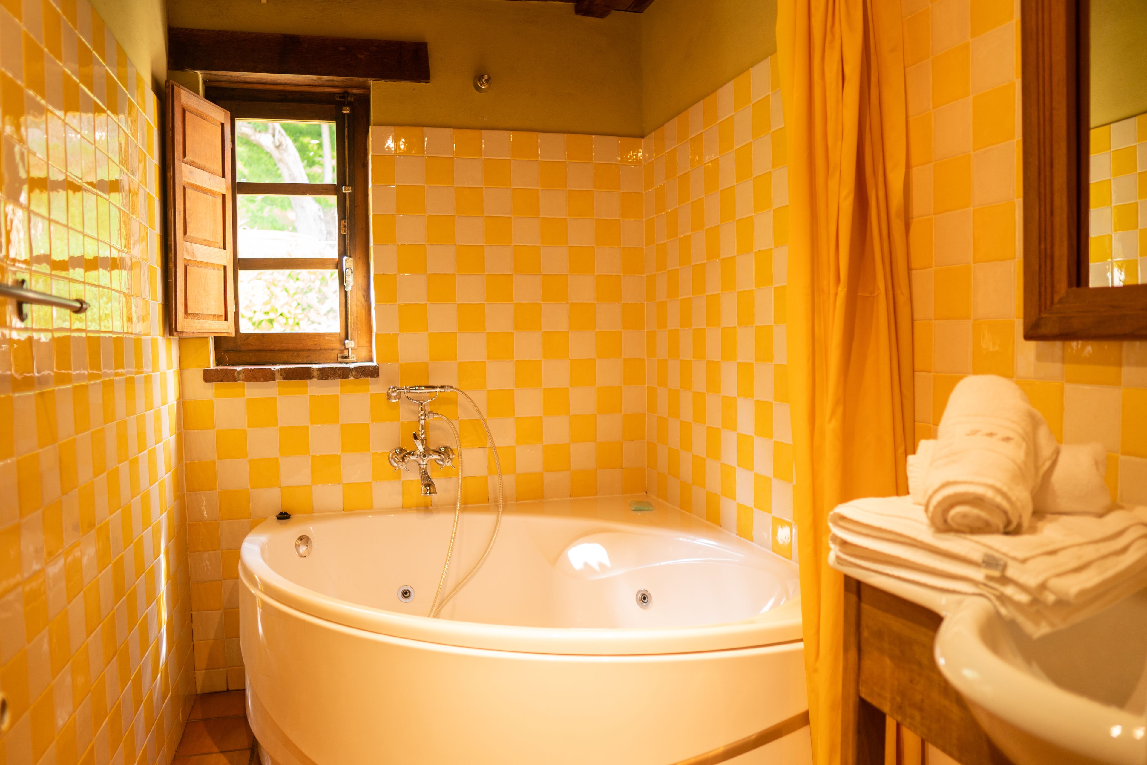 Un baño con baldosas amarillas a cuadros, una bañera, una ventana y un perchero para toallas.
