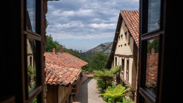 Un camí empedrat i estret flanquejat per edificis tradicionals amb teulades ceràmiques, que s'adreça cap a un paisatge de muntanya.