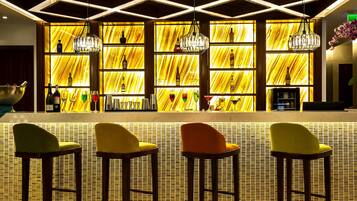 A bar area with a unique yellow patterned wall, wooden bar stools, and hanging crystal chandeliers.