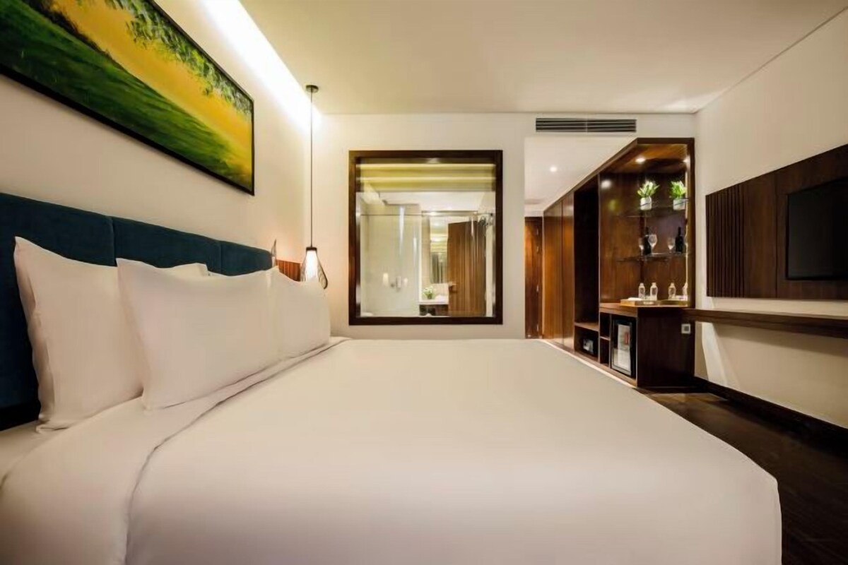 A hotel room with a large bed, a TV, a desk, and a bathroom visible through an open door.