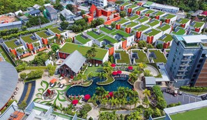 An aerial view of a modern hotel with rooftop gardens, a central swimming pool, and multiple buildings with distinct architectural styles. - MIDA Grande Resort Phuket (Choeng Thale)