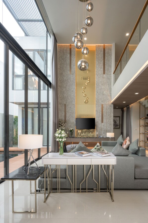 A modern living room with a sofa, a coffee table, and a TV mounted on the wall. - MIDA Grande Resort Phuket (Choeng Thale)