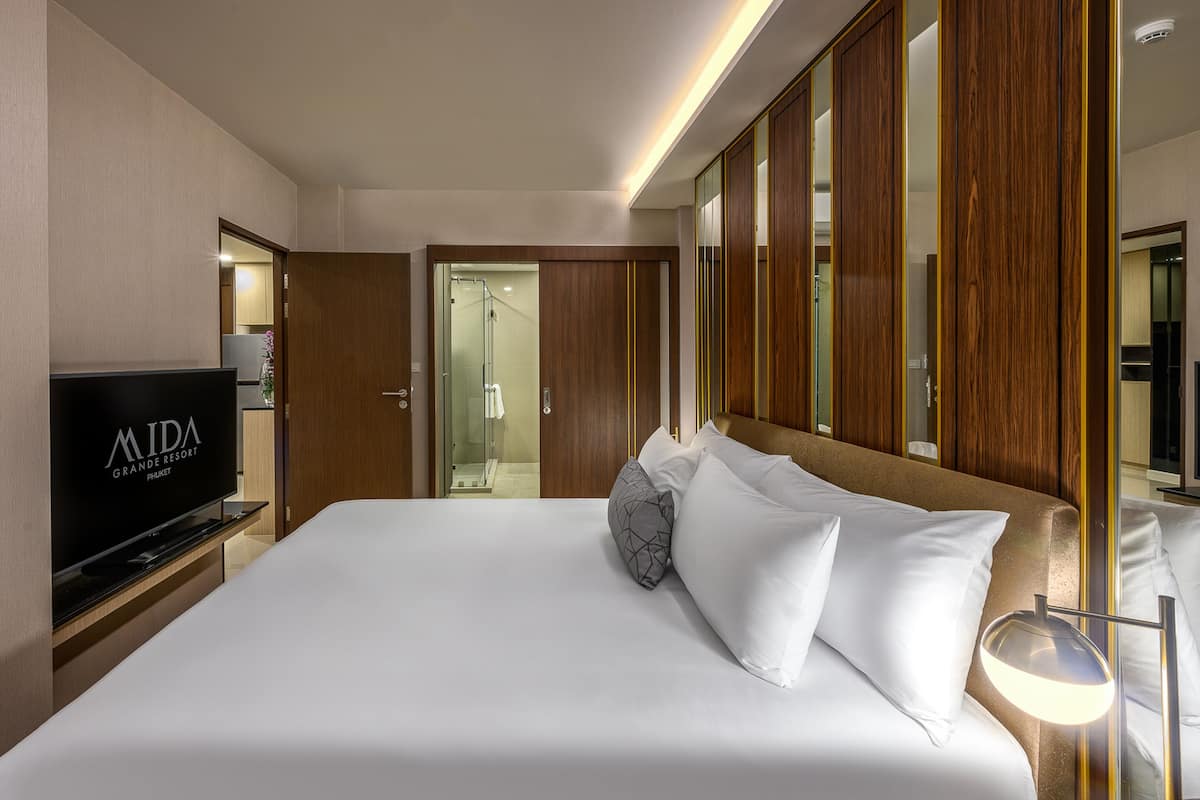 A hotel room with a large bed, a TV, wooden paneling, and a bathroom visible through an open door.