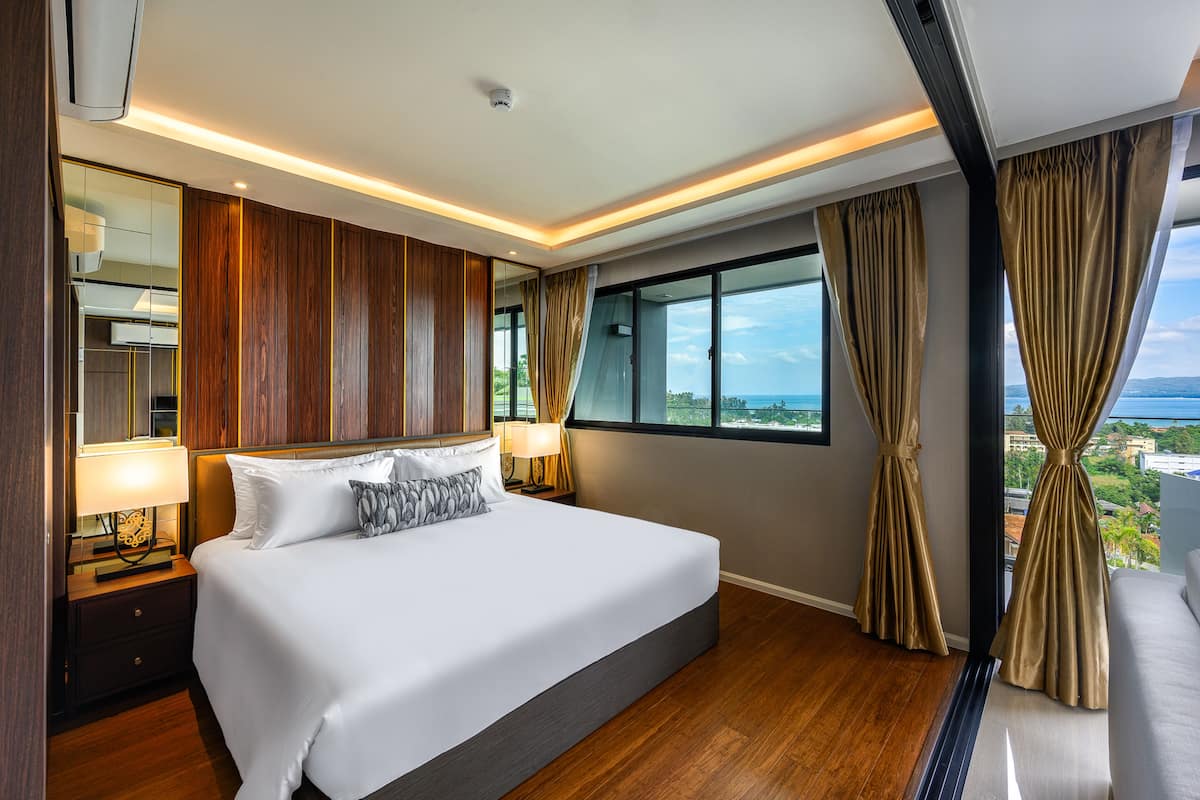 A modern hotel room with a large bed, wooden paneling, a view of the ocean, and a balcony.
