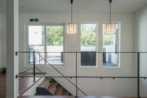 A staircase with a metal railing, a wooden floor, and a view of the outdoors through large windows. - Lux Terrace Okinawa (Onna)