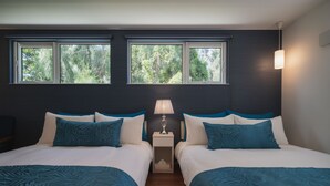A hotel room with two beds, a nightstand with a lamp, and a view of trees through large windows. - Lux Terrace Okinawa (Onna)