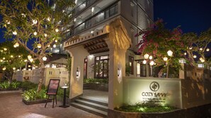 Entrada de un hotel boutique con una señal, escalones que llevan a la entrada e iluminación decorativa.