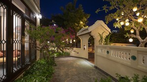 Un patio con un sendero adoquinado, un arco decorativo y un árbol con luces colgantes.