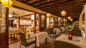 Un restaurante con mesas dispuestas para comer, sillas de mimbre y faroles colgantes.