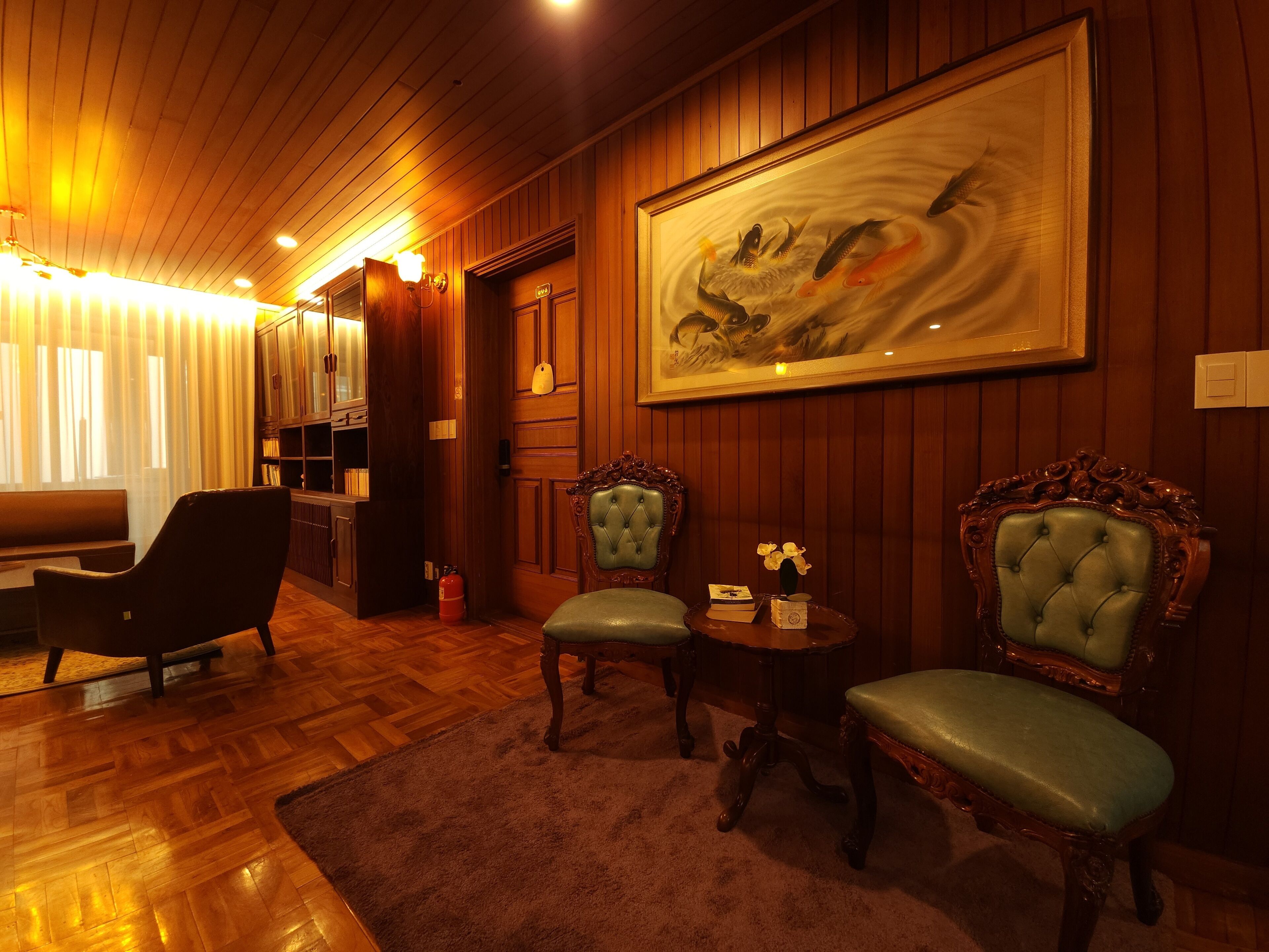 A cozy room with wooden paneling, a large painting of fish, and two green upholstered chairs.