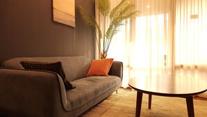 A modern living room with a grey sofa, a round coffee table, and a large potted plant. - OYO Hostel Myeongdong 5 (Seoul)