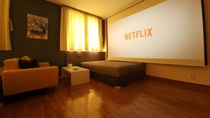 A modern hotel room with a wooden floor, a bed, a small bedside table with a plant, a couch, and a large screen displaying the Netflix logo. - OYO Hostel Myeongdong 5 (Seoul)