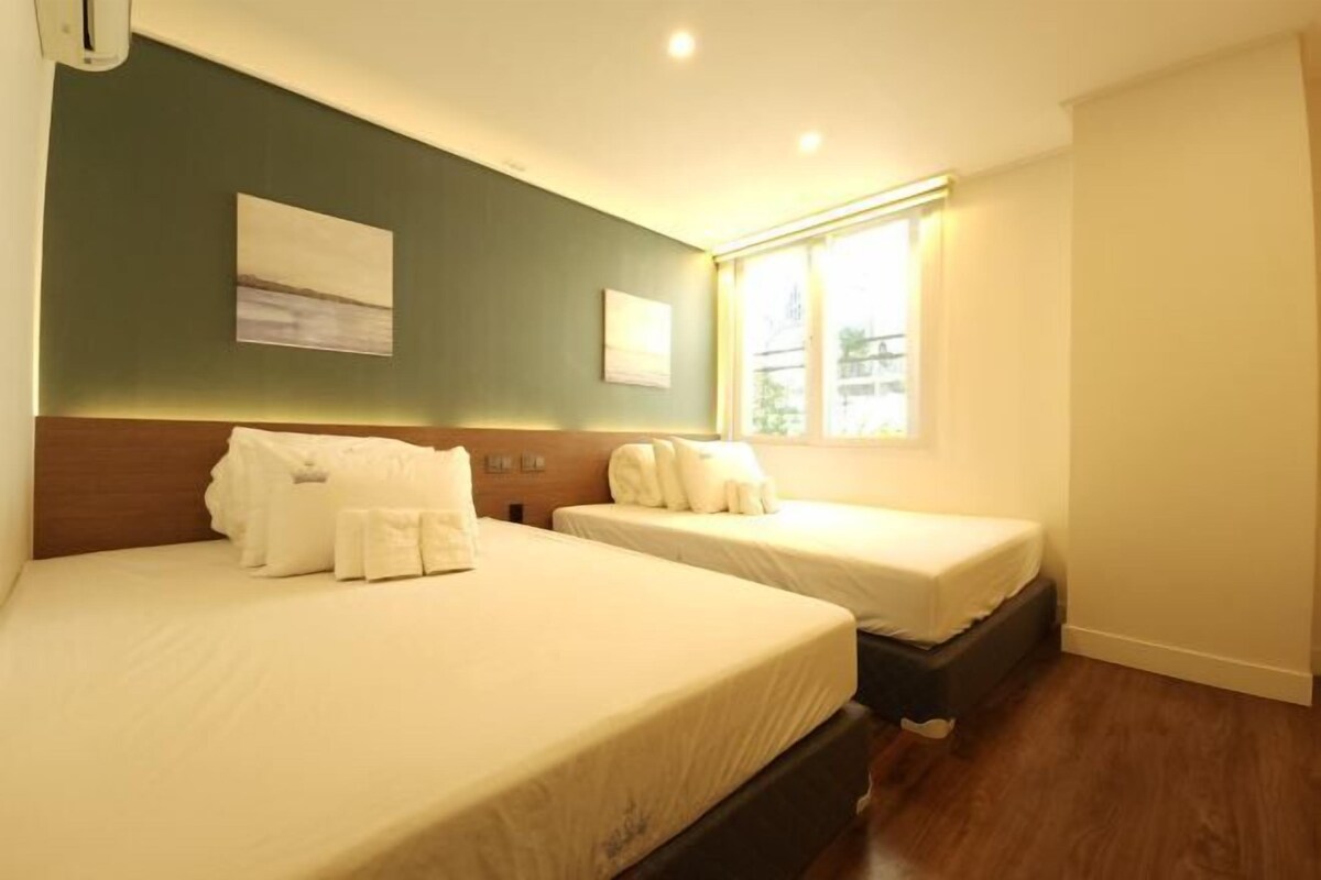 Habitación de hotel con dos camas, cabecera, ventana con cortinas y una obra de arte en la pared.
