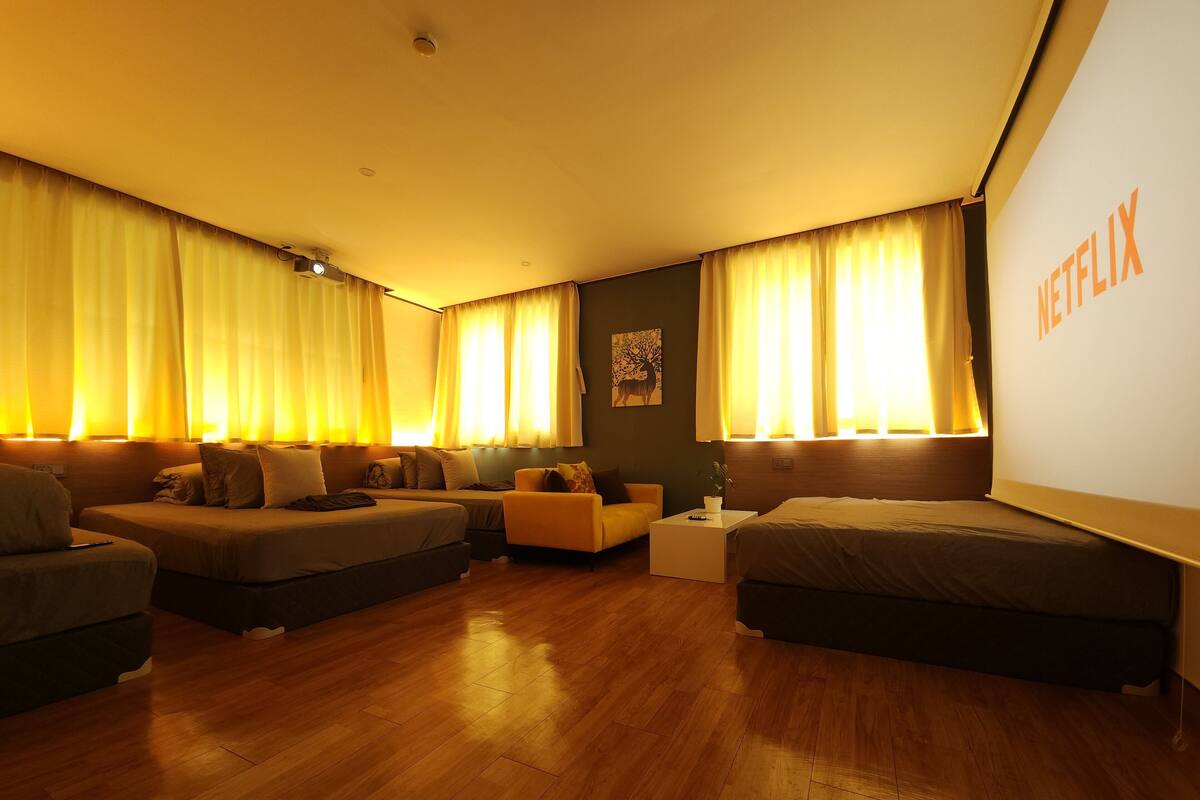 Habitación de hotel con dos camas, un sofá, una mesita pequeña y un ventanal con cortinas.