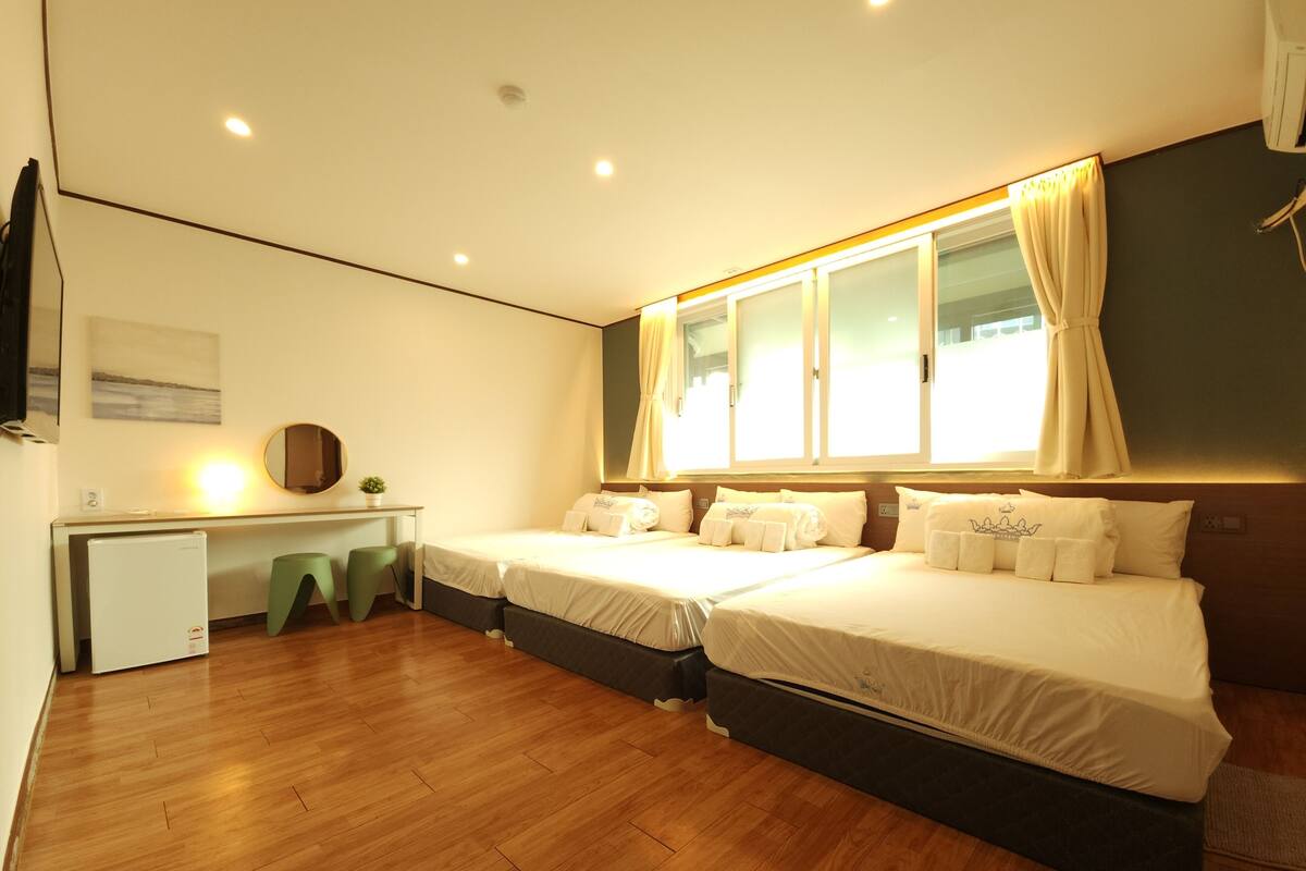 Una habitación de hotel con dos camas, un escritorio, un espejo y una ventana con cortinas.