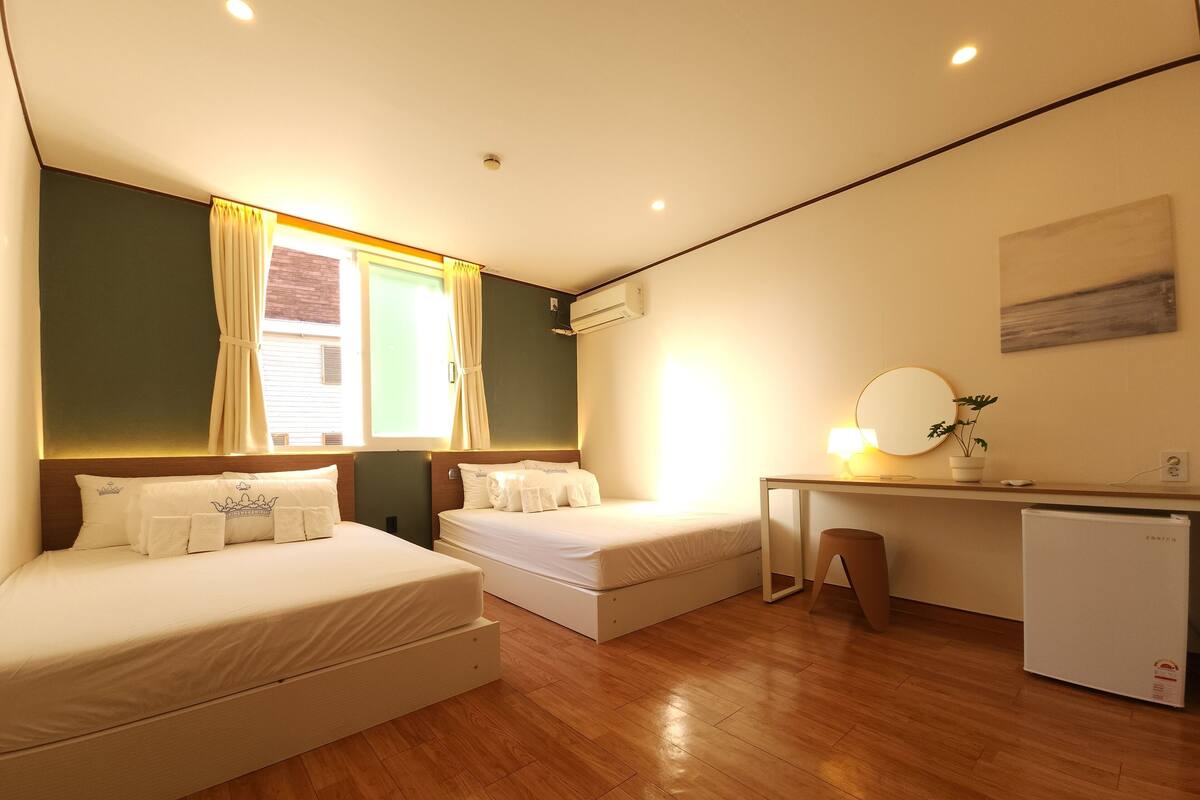 Habitación de hotel con dos camas, un escritorio, un refrigerador pequeño y una ventana con cortinas.
