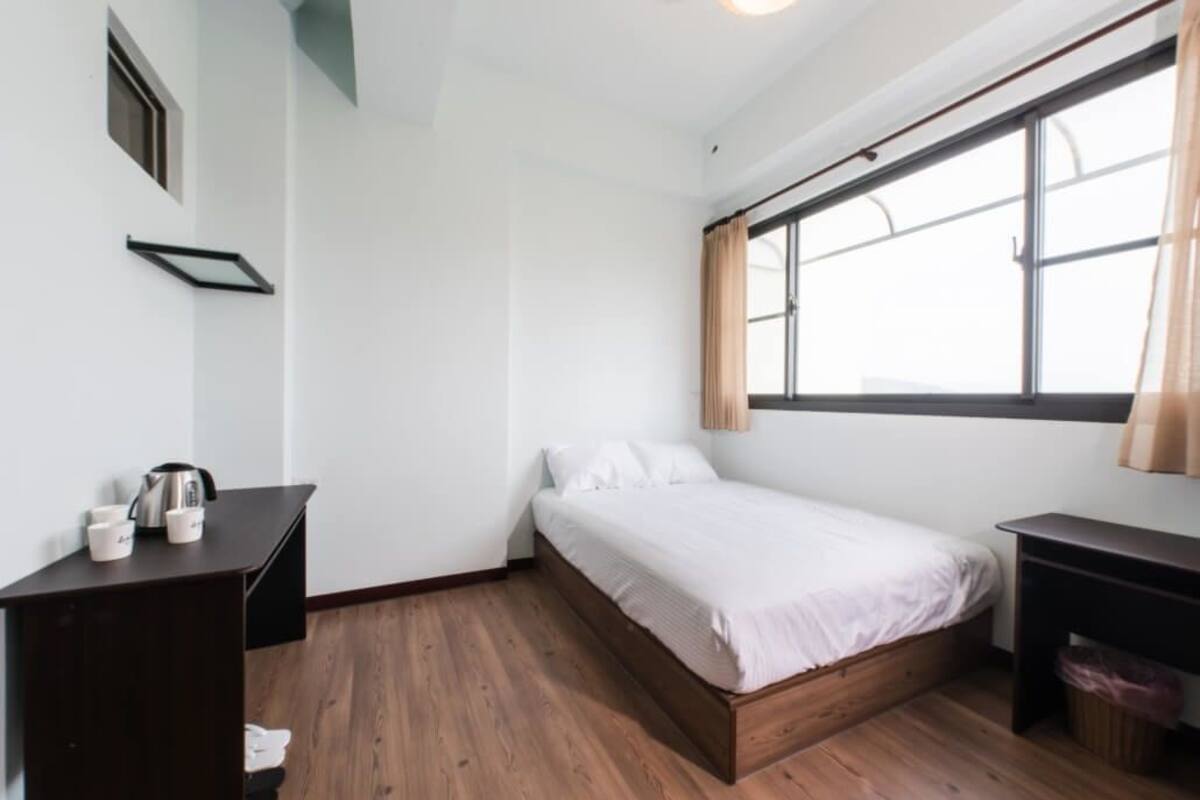 Une petite pièce propre, avec un lit simple, un bureau et une fenêtre.