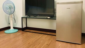 A room with a flat-screen TV on a stand, a small refrigerator, and a standing fan. - Yujing Mountain Water Residence I (Tainan)