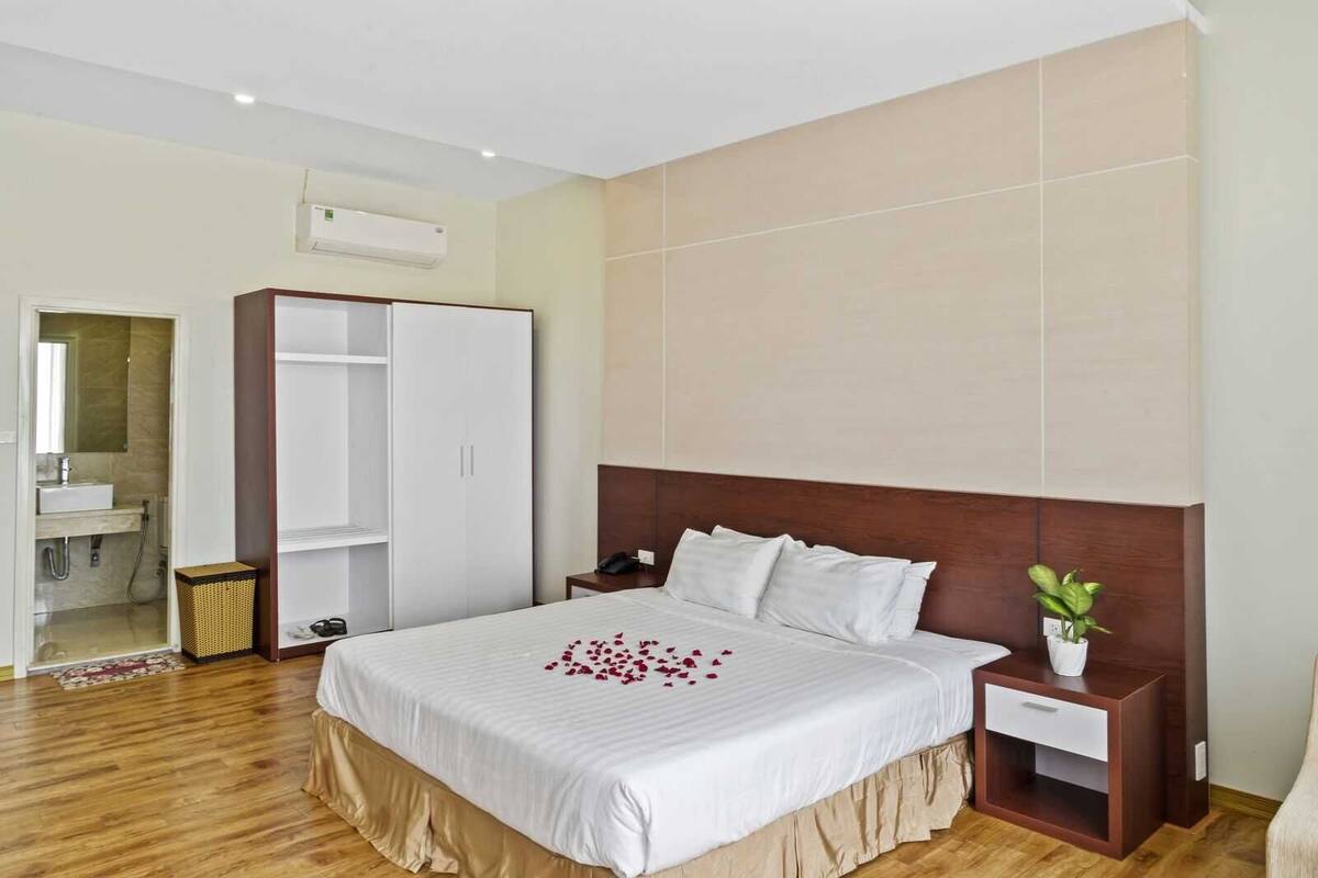 A hotel room with a large bed, a wardrobe, a bedside table, and a small plant.