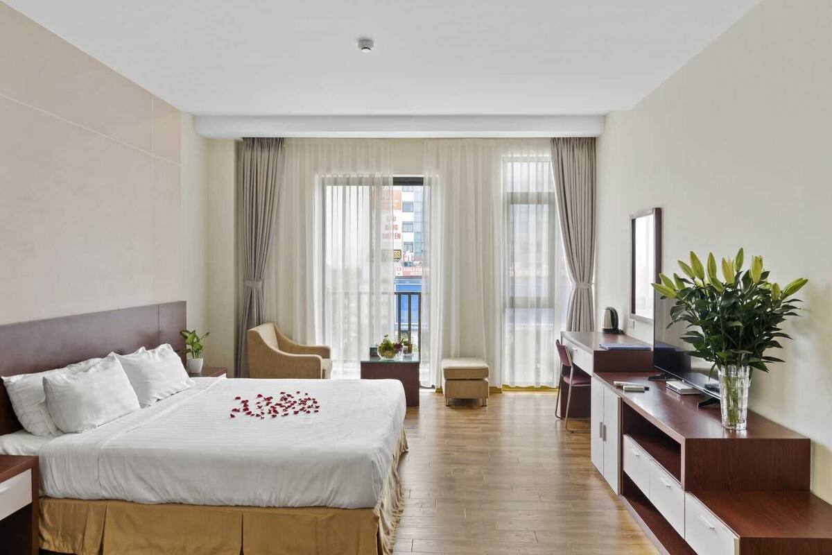 A hotel room with a bed, a desk, a chair, and a view of the city.