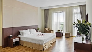 A hotel room with a large bed, a nightstand, a chair, a small table, and a potted plant. - Nara Hotel (Kinh Bac)