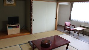 Une pièce de style japonais traditionnel, avec un sol recouvert de tatamis, une petite table sur laquelle se trouve un objet rond, un téléviseur posé sur un meuble et une chaise avec un coussin.