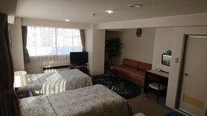 Une chambre d’hôtel avec deux lits, une télévision, un canapé, un bureau et une fenêtre avec des rideaux.