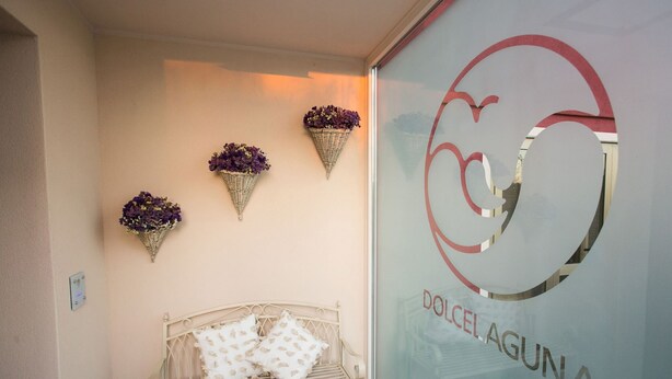 A bench with cushions, a wall-mounted basket with flowers, and a glass wall with a logo and text. - Dolce Laguna (Mestre)