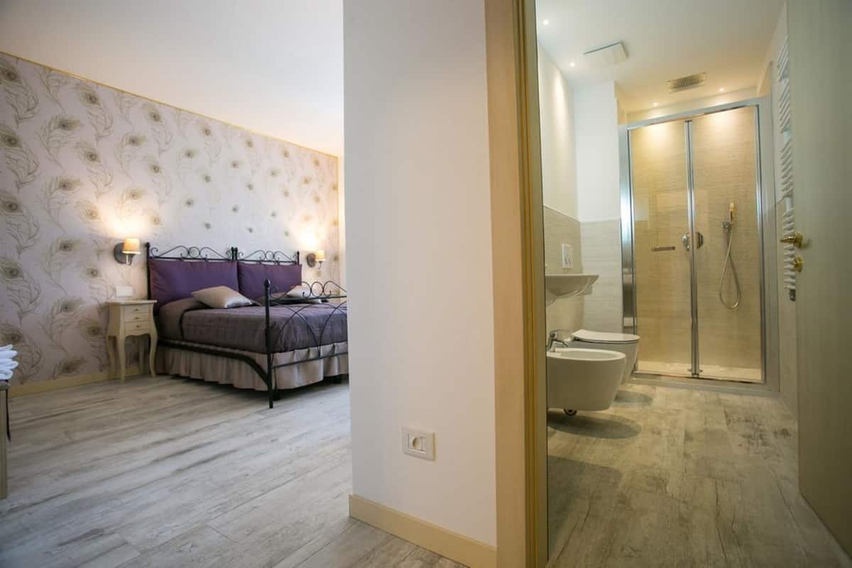 A bedroom with a bed, bedside tables, and a bathroom with a shower, toilet, and bathtub.