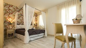 A bedroom with a four-poster bed, a wooden chair, a bedside table, and a wall with floral wallpaper. - Dolce Laguna (Mestre)