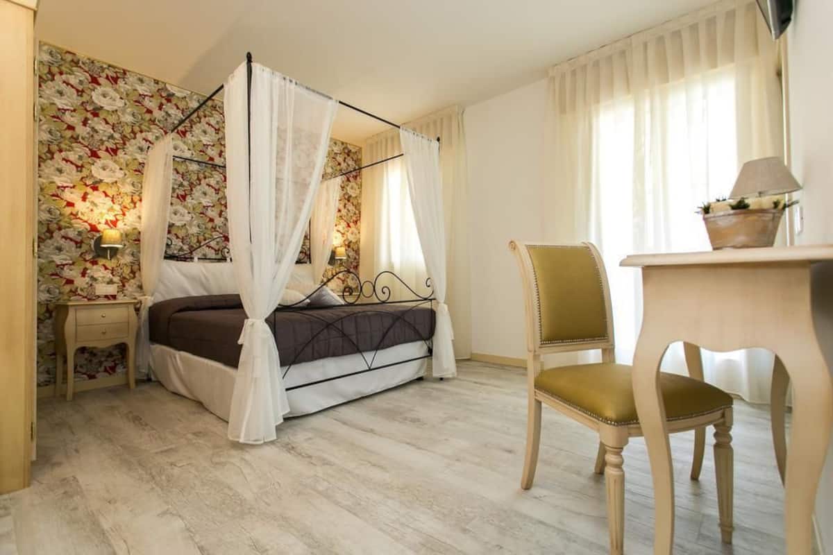 A bedroom with a four-poster bed, a wooden chair, a bedside table, and a wall with floral wallpaper.
