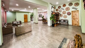 A spacious lobby with a high ceiling, a central seating area with sofas and a coffee table, a reception desk, and a wall decorated with circular patterns. - Hotel Moloka’I Morotai (Morotai Island)