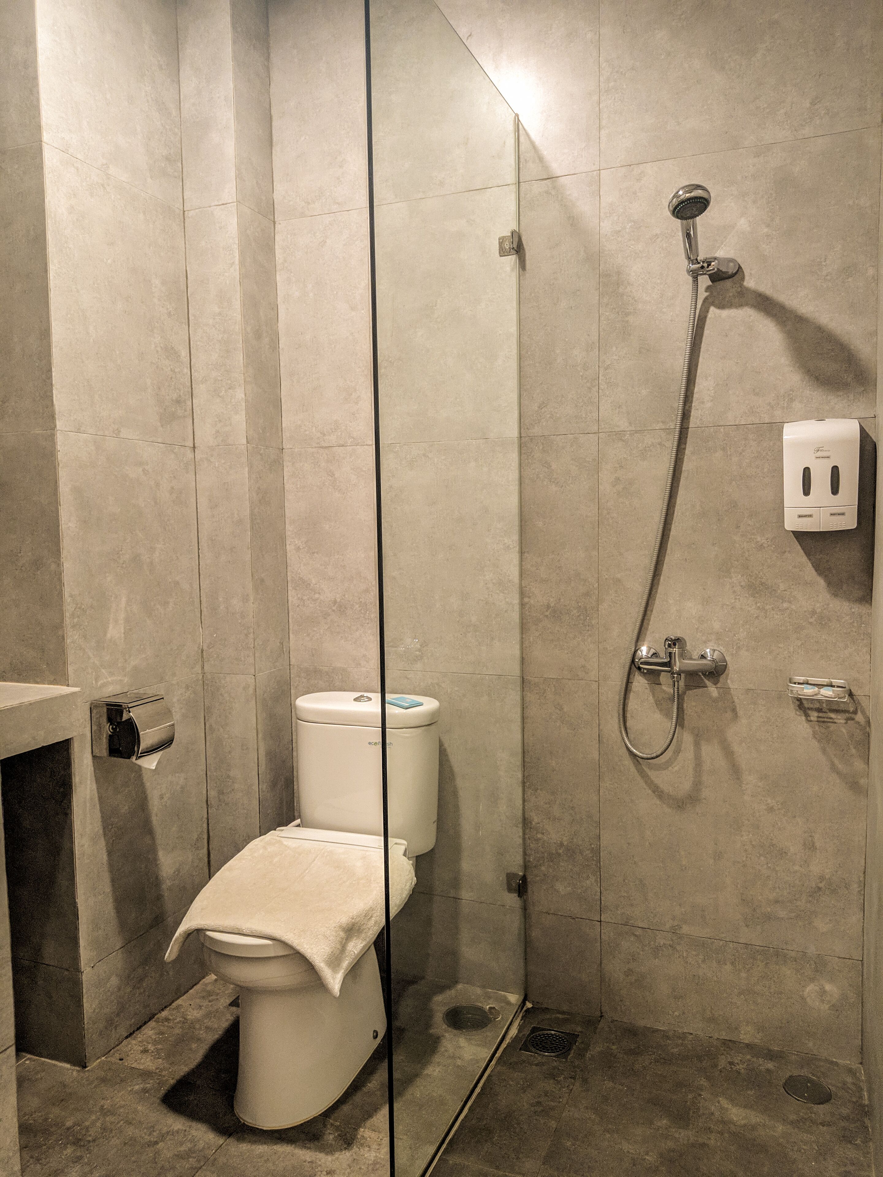 A modern bathroom with a glass-enclosed shower, a toilet, and a hand dryer.
