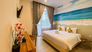 A bedroom with a bed, a desk with a vase of flowers, a painting of a beach, and a view of the outdoors. - Hotel Moloka’I Morotai (Morotai Island)