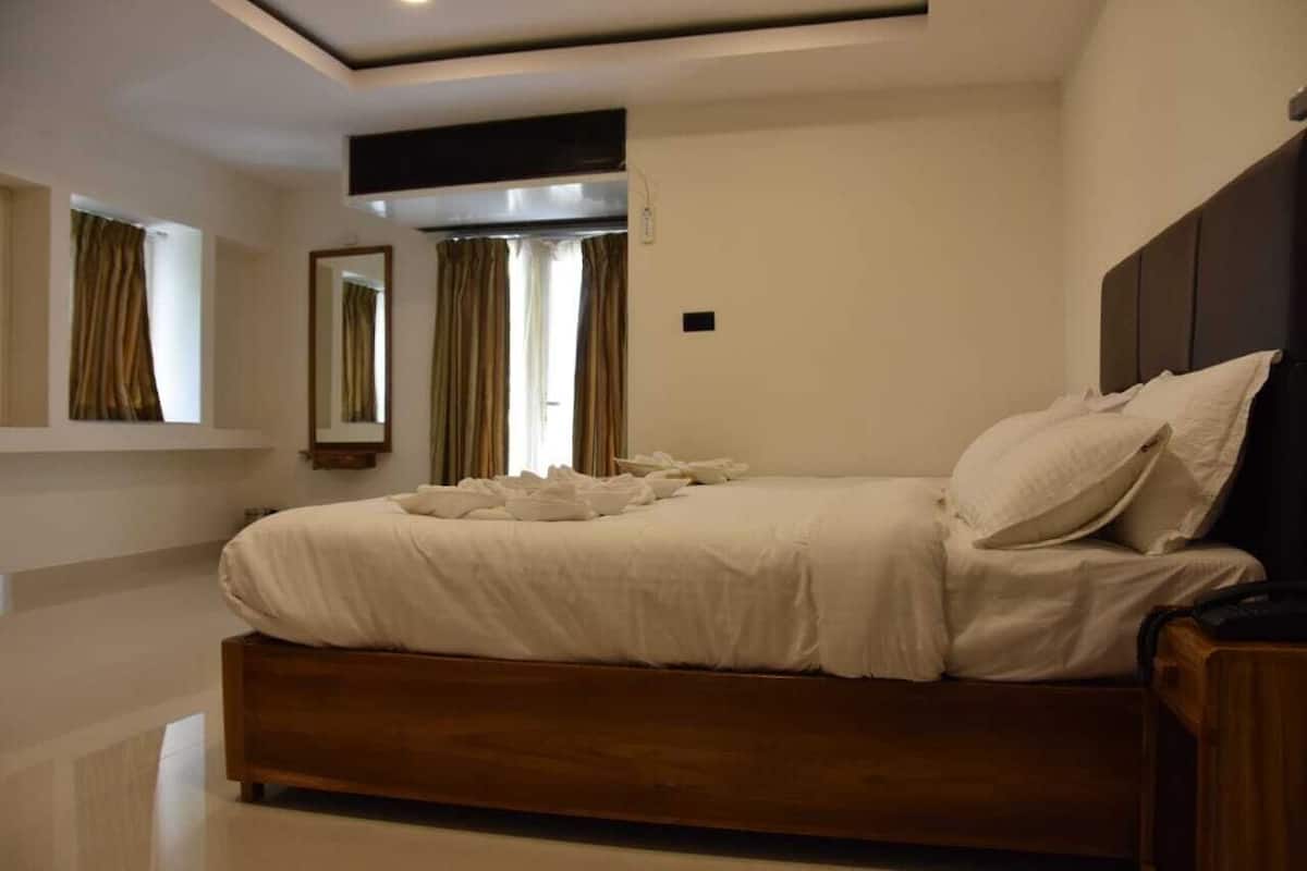 A bedroom with a large bed, a bedside table, a mirror, and a window with curtains.