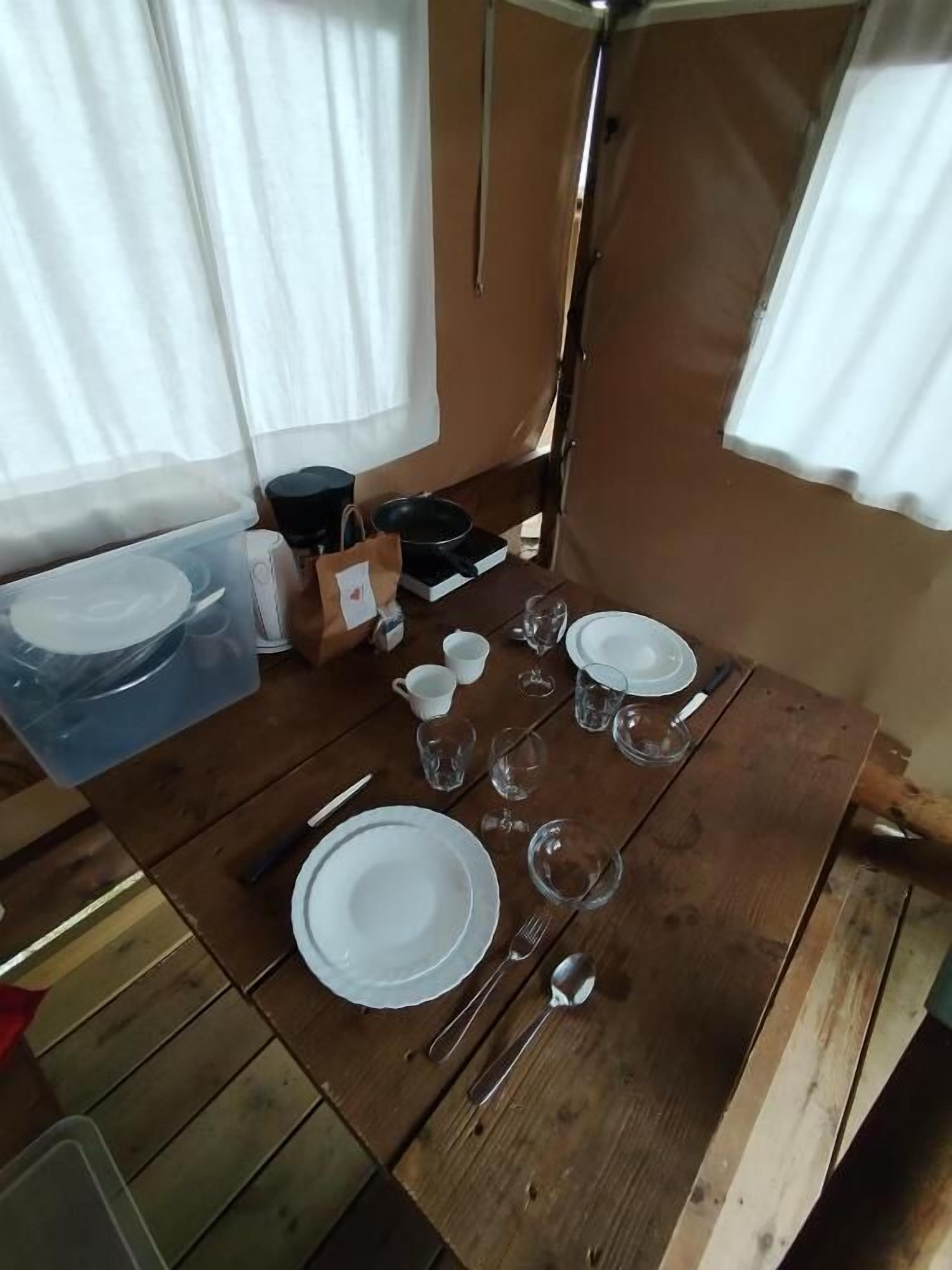Una mesa de comedor de madera dispuesta con platos blancos, cubiertos y vasos transparentes.