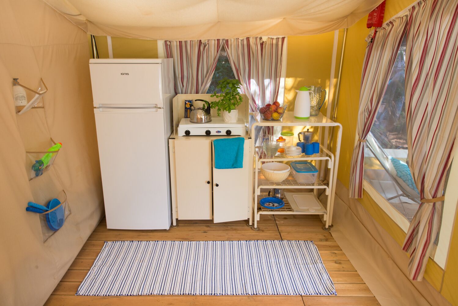 A compact kitchen with a white refrigerator, a gas stove, and a small shelf with dishes and a kettle.